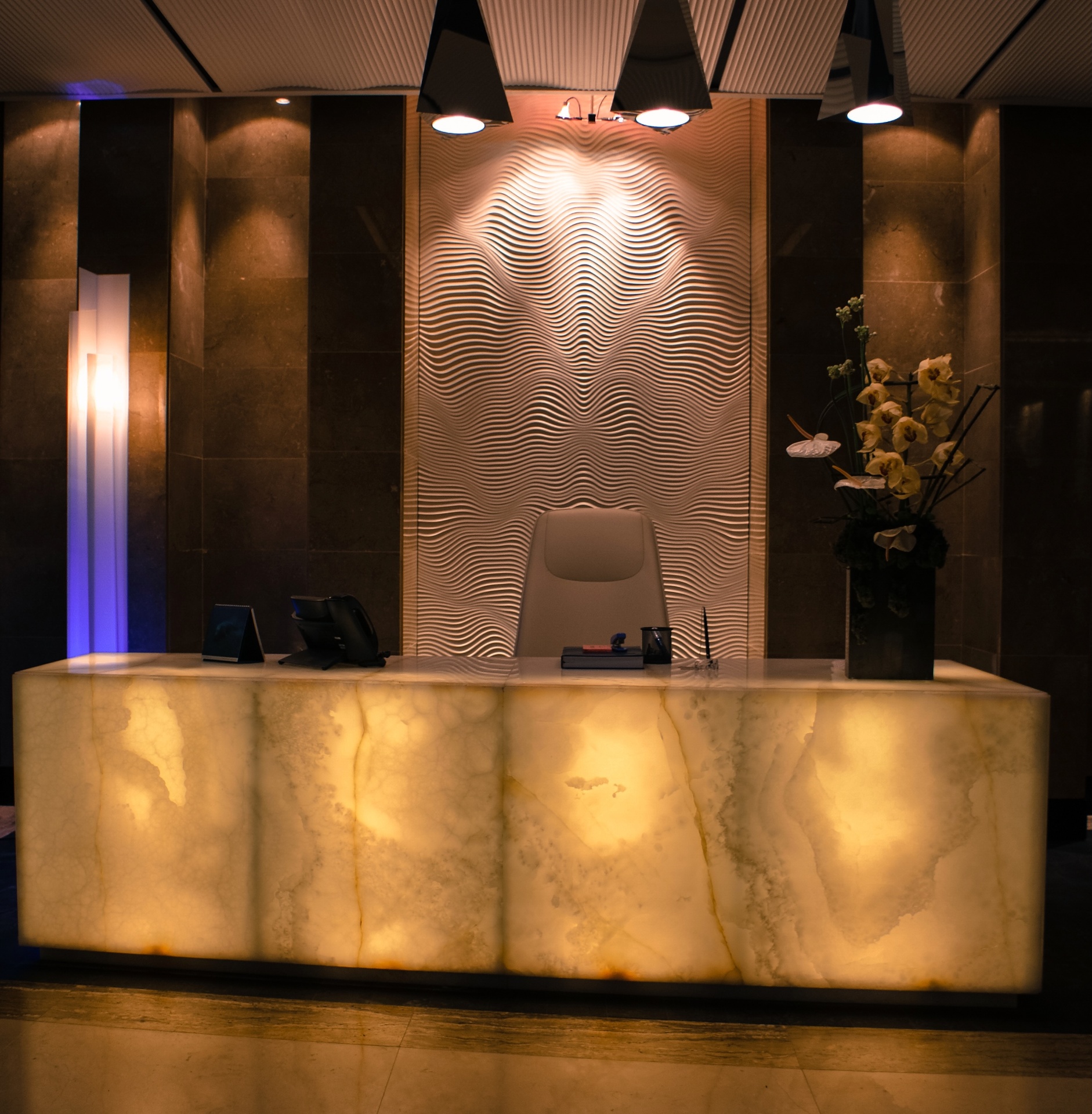 Luxury hotel reception with 3D CNC carved wave pattern wall panel and backlit onyx desk
